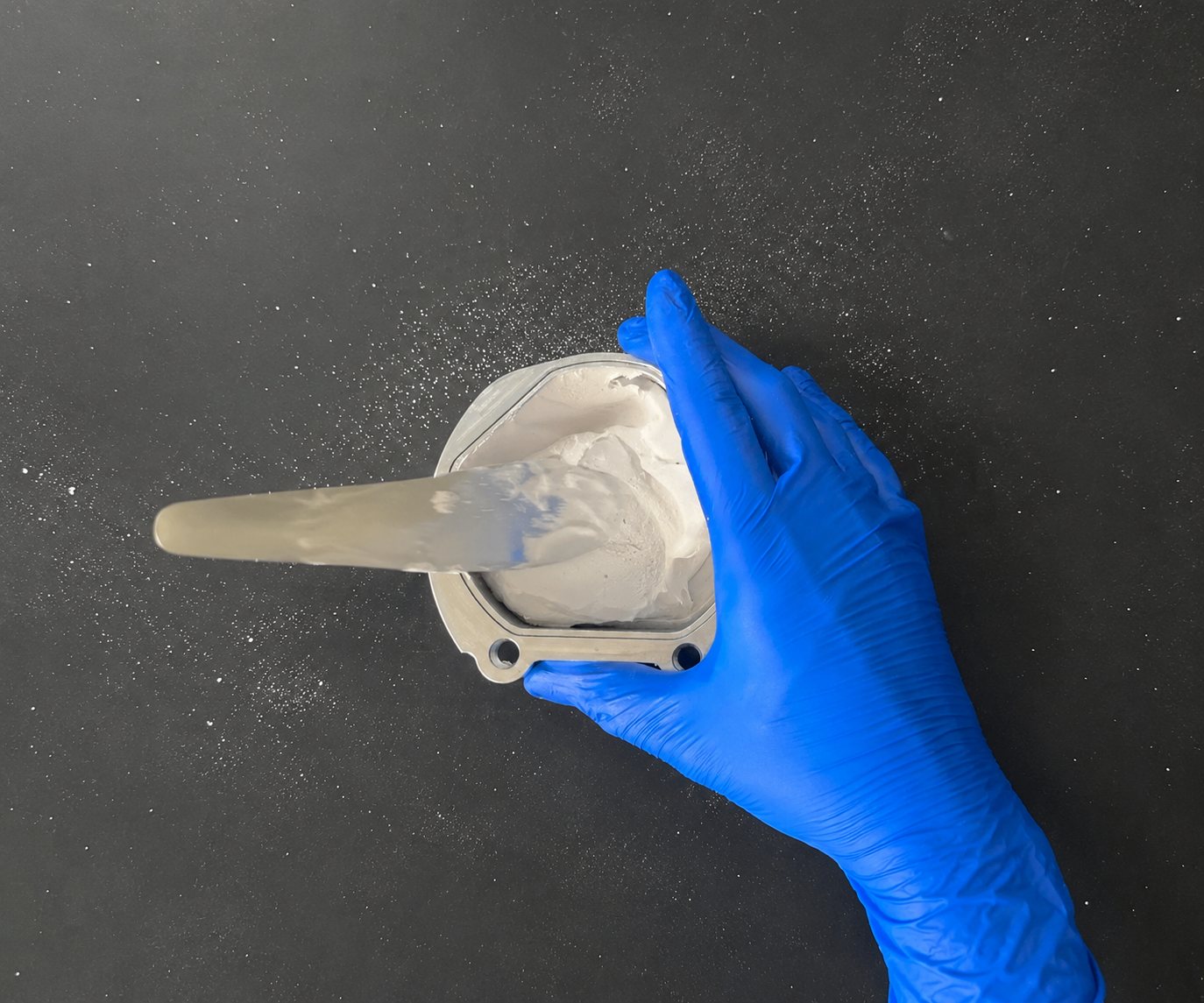 Gloved hand mixing white plaster in a LabPilot flask with a spatula