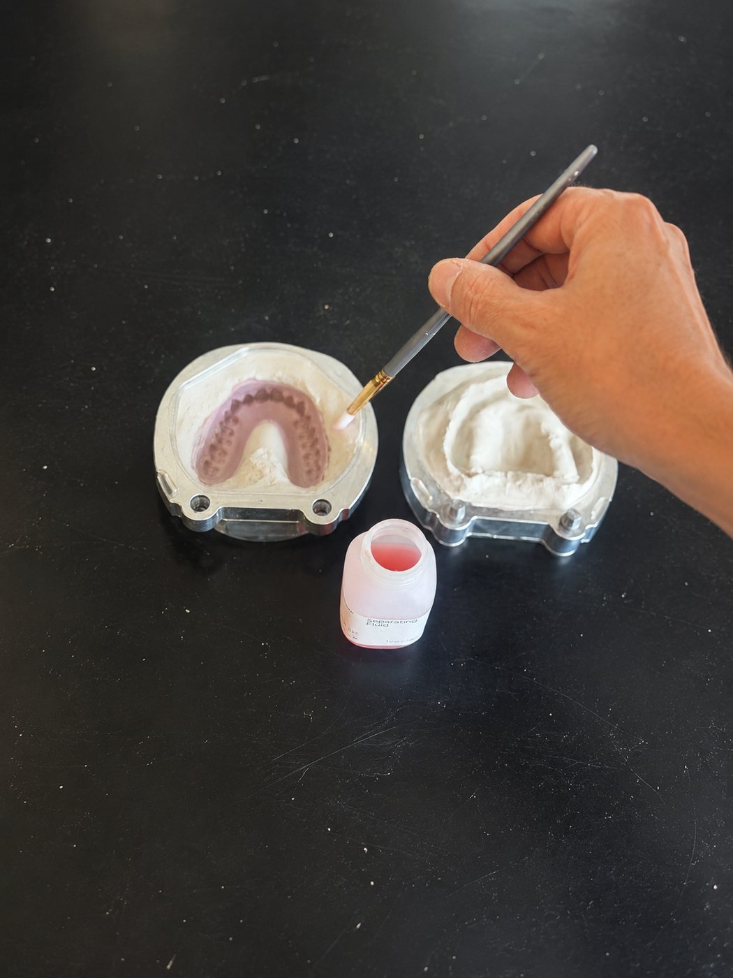 Brush painting separator on plaster around a wax-up, with separating fluid nearby